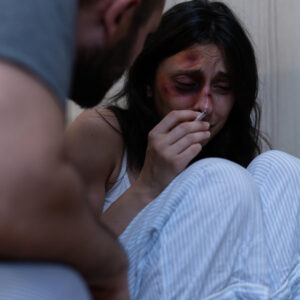 Kobieta doświadczająca przemocy domowej, siedząca na podłodze, wyraźnie przestraszona i z obrażeniami twarzy.