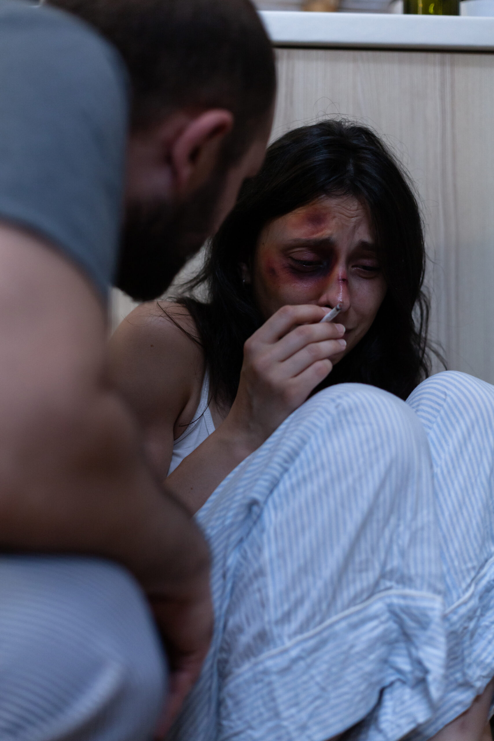 Kobieta doświadczająca przemocy domowej, siedząca na podłodze, wyraźnie przestraszona i z obrażeniami twarzy.